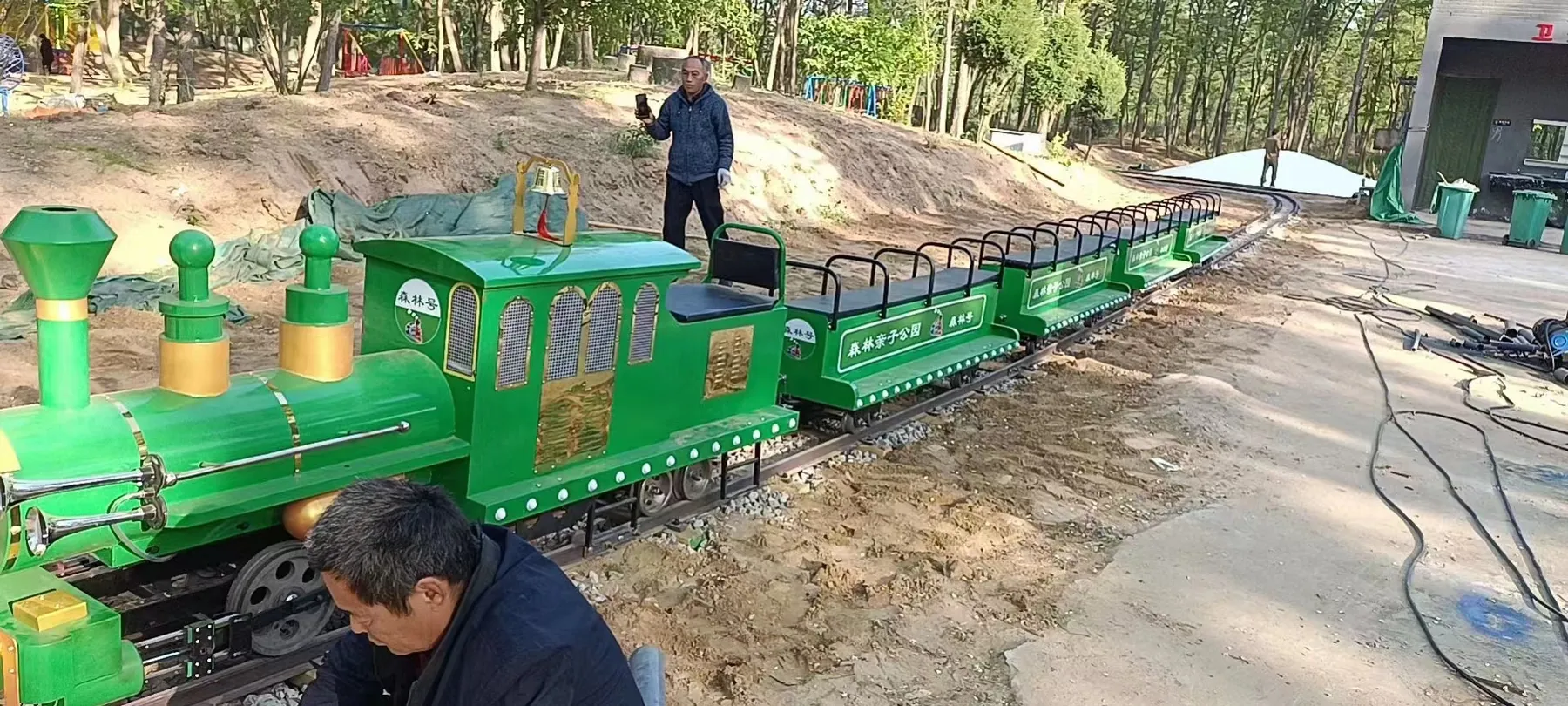 Trackless vs Track Train: Specs, Costs & How to Choose Green track sightseeing train being installed on a newly laid rail loop at a forest park
